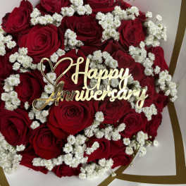 Red roses with white baby's breath and a gold Happy Anniversary topper