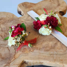 Two floral boutonnieres with red and white roses on a wooden surface