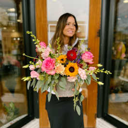 Woman holding a colorful mixed flower arrangement in a textured container