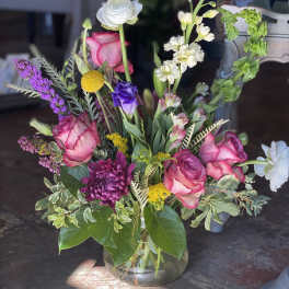 Mixed bouquet of pink roses, white blooms, and purple flowers in a glass vase
