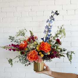 Colorful mixed bouquet in a gold vase with orange, blue, and magenta flowers