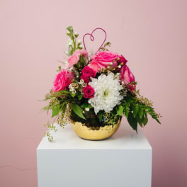 Pink and white flower arrangement in a gold bowl with a heart pick