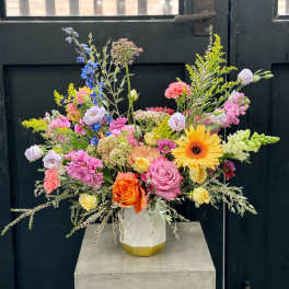 Mixed bouquet in a white vase with pink, yellow, orange, and blue flowers