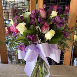 Bouquet of pink, white, and purple flowers in a glass vase with a lavender ribbon