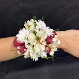 White floral wrist corsage with burgundy ribbon on a person’s wrist