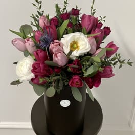 Pink and white tulip bouquet in a black hatbox with greenery