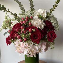 Bouquet of red roses, white carnations, and pink berries in a green glass vase