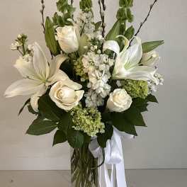 White lilies and roses arranged in a clear glass vase with a white ribbon