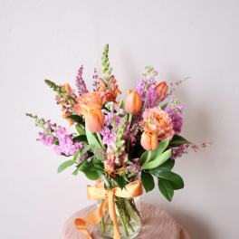 Orange and pink mixed bouquet in a clear glass vase with ribbon