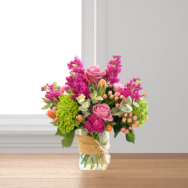 Pink roses and magenta flowers in a glass vase with burlap ribbon