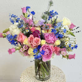 Colorful mixed bouquet of pink, blue, and white flowers in a glass vase