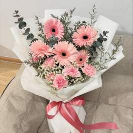Pink gerbera daisy bouquet wrapped in white paper with a pink ribbon