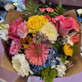 Colorful mixed bouquet with roses, gerbera daisies, and chrysanthemums wrapped in brown paper