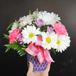 Pink and white daisy bouquet in a purple vase with a plaid ribbon