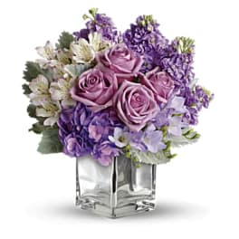 Lavender roses and purple flowers in a clear square vase