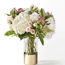 White and blush bouquet in a clear glass vase with a gold base
