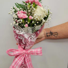 Pink carnations and a white rose in a wrapped bouquet with a pink ribbon