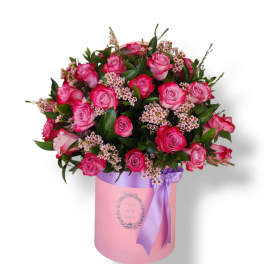 Pink roses arranged in a round box with a purple ribbon