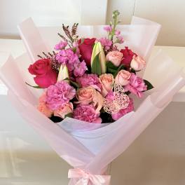 Pink and peach rose bouquet with carnations and lilies in pale pink wrap
