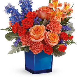 Mixed bouquet of roses, carnations, and blue flowers in a blue vase