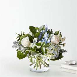 White roses and blue flowers in a clear glass vase