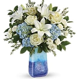 White lilies and roses arranged with blue hydrangeas in a blue glass vase