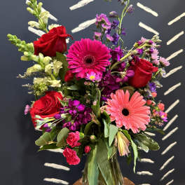 Mixed bouquet of red roses, pink gerbera daisies, and purple flowers in a glass vase