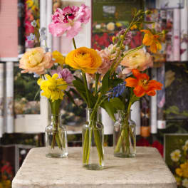 Three small glass vases hold colorful mixed flowers on a stone pedestal.