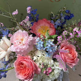 Bouquet of pink roses, peonies, and blue flowers in a wrapped arrangement