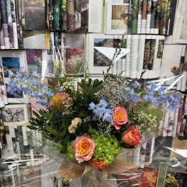 Mixed bouquet of orange and pink roses with blue flowers in a glass vase