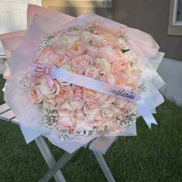 Large bouquet of pale pink roses wrapped in pink paper with a ribbon