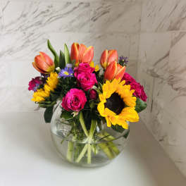 Bouquet of tulips, roses, and sunflowers in a round glass vase