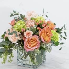 Peach and coral roses in a clear glass vase with green filler flowers