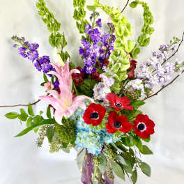 Tall bouquet of pink lilies, red anemones, and purple blooms in a glass vase