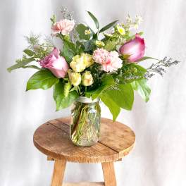 Pink and yellow roses with carnations in a glass jar vase