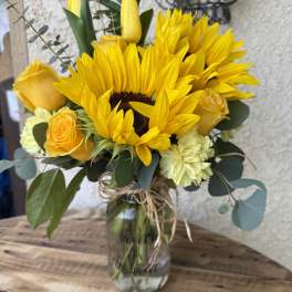 Yellow sunflower bouquet in a glass jar with roses and carnations