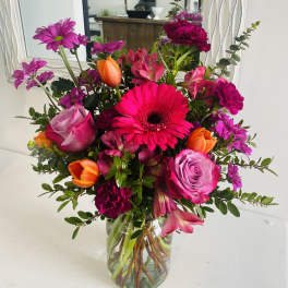 Bright mixed bouquet in a clear glass vase with pink, orange, and purple flowers