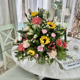 Mixed bouquet with sunflowers, pink carnations, and white daisies in a glass vase