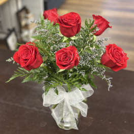 Red roses arranged in a clear glass vase with a white ribbon.
