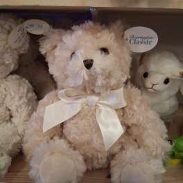 Plush teddy bear with a white ribbon bow sitting on a shelf