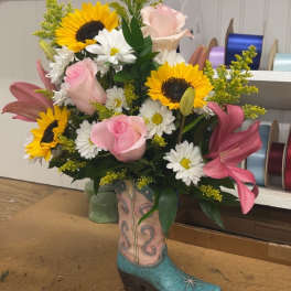 Bouquet in a decorative cowboy boot vase with sunflowers, pink roses, lilies, and daisies