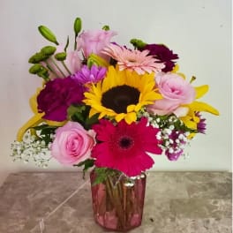 Mixed bouquet with sunflowers, gerbera daisies, roses, and lilies in a pink vase