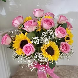 Pink roses and sunflowers arranged in a glass vase with baby's breath