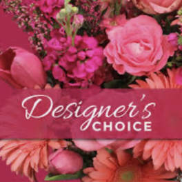 Pink floral arrangement with roses and daisies behind a Designer's Choice label