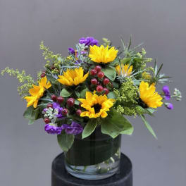 Yellow sunflowers and purple flowers in a glass vase