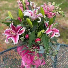 Pink lilies and snapdragons in a glass vase with a pink ribbon