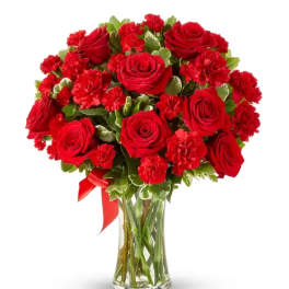 Red roses and carnations in a clear glass vase with a red ribbon
