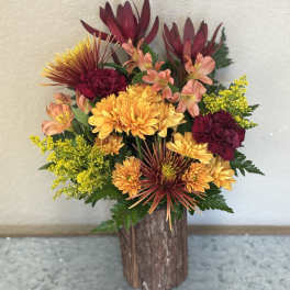 Mixed bouquet of orange, burgundy, and yellow flowers in a rustic wooden vase