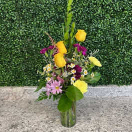 Mixed bouquet in a clear glass vase with yellow roses and purple flowers