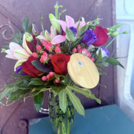 Bouquet of red roses, pink lilies, and purple blooms in a glass vase